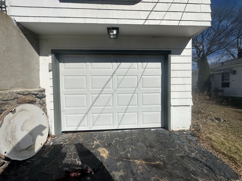 White raised-panel garage door on white home with green trim and stone foundation